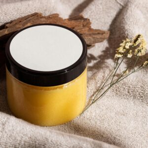 Jar of yellow skincare cream on a towel with wood and dried flowers, ideal for spa themes.