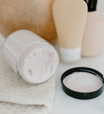 Glass jar with face cream amidst gentle skincare products on a neutral background.