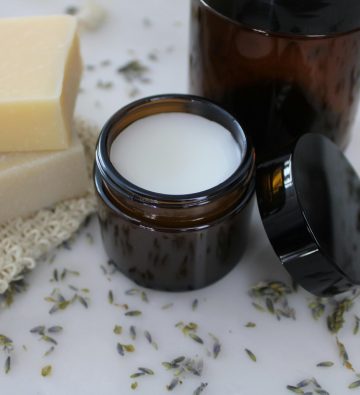 Organic bar soap and skin cream in amber jars with lavender sprigs on marble.